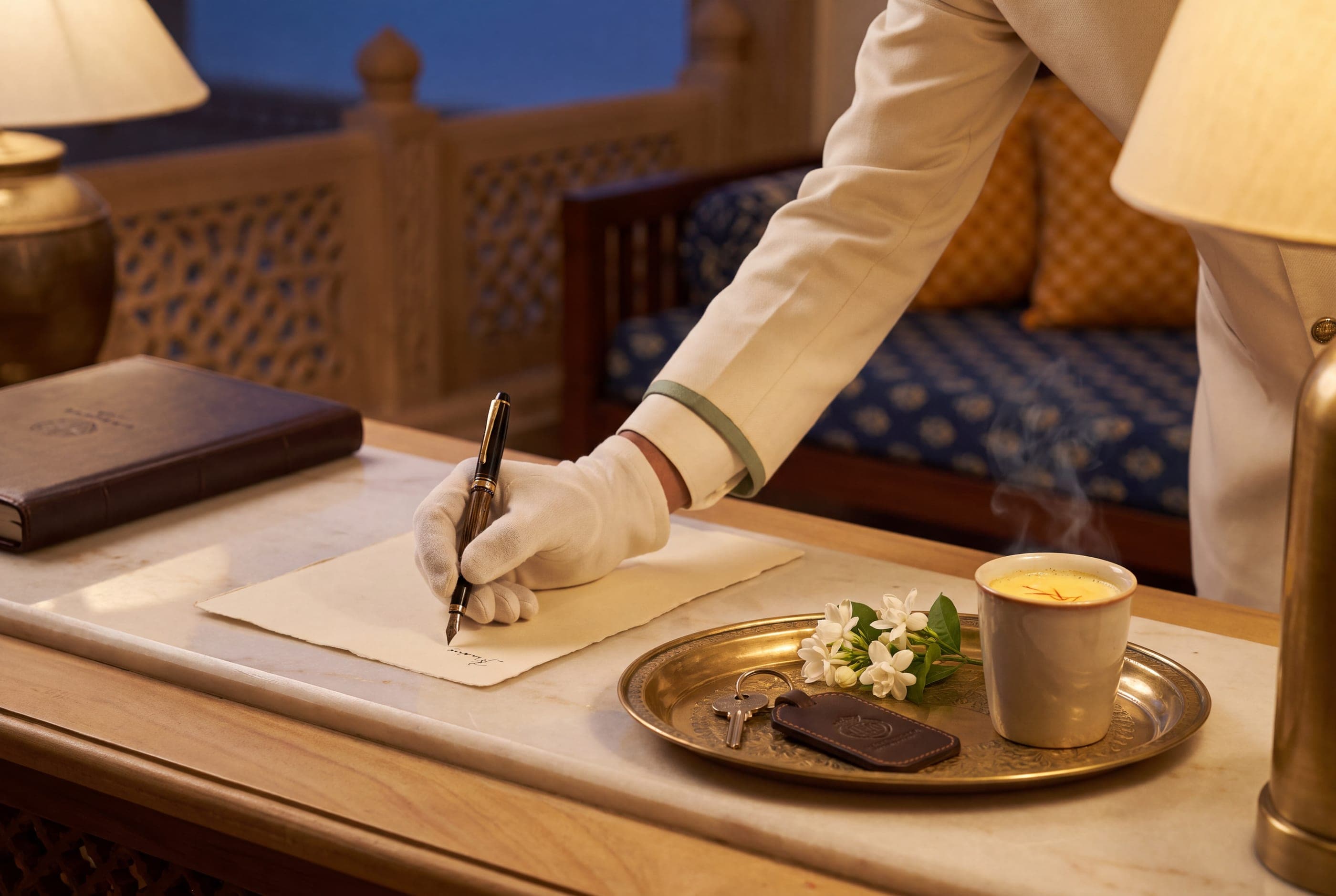 A concierge writing a handwritten welcome note beside a room key and a cup of saffron milk