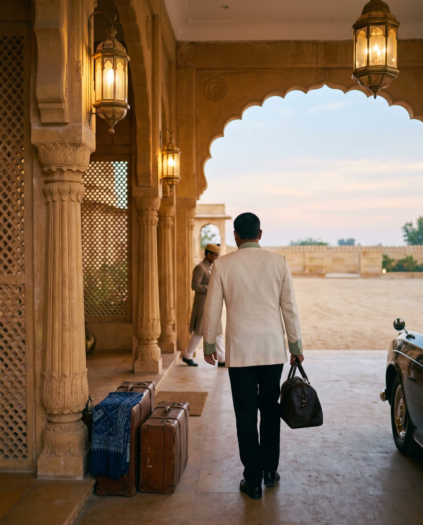 At first light, a staff member carries a bag out under the entrance porch, past two waiting suitcases