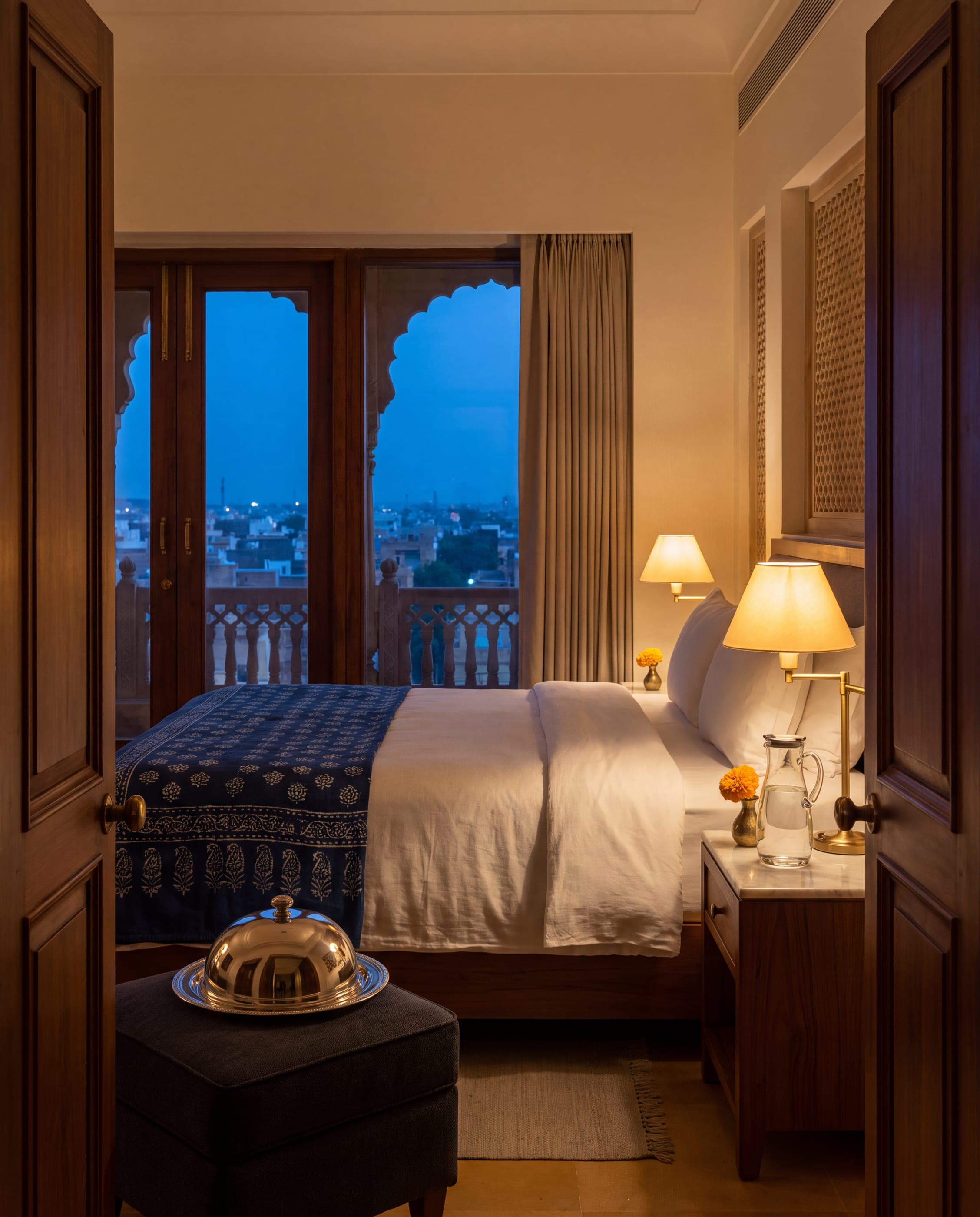 A hotel room prepared for a late arrival, with a covered supper tray waiting at the foot of the bed